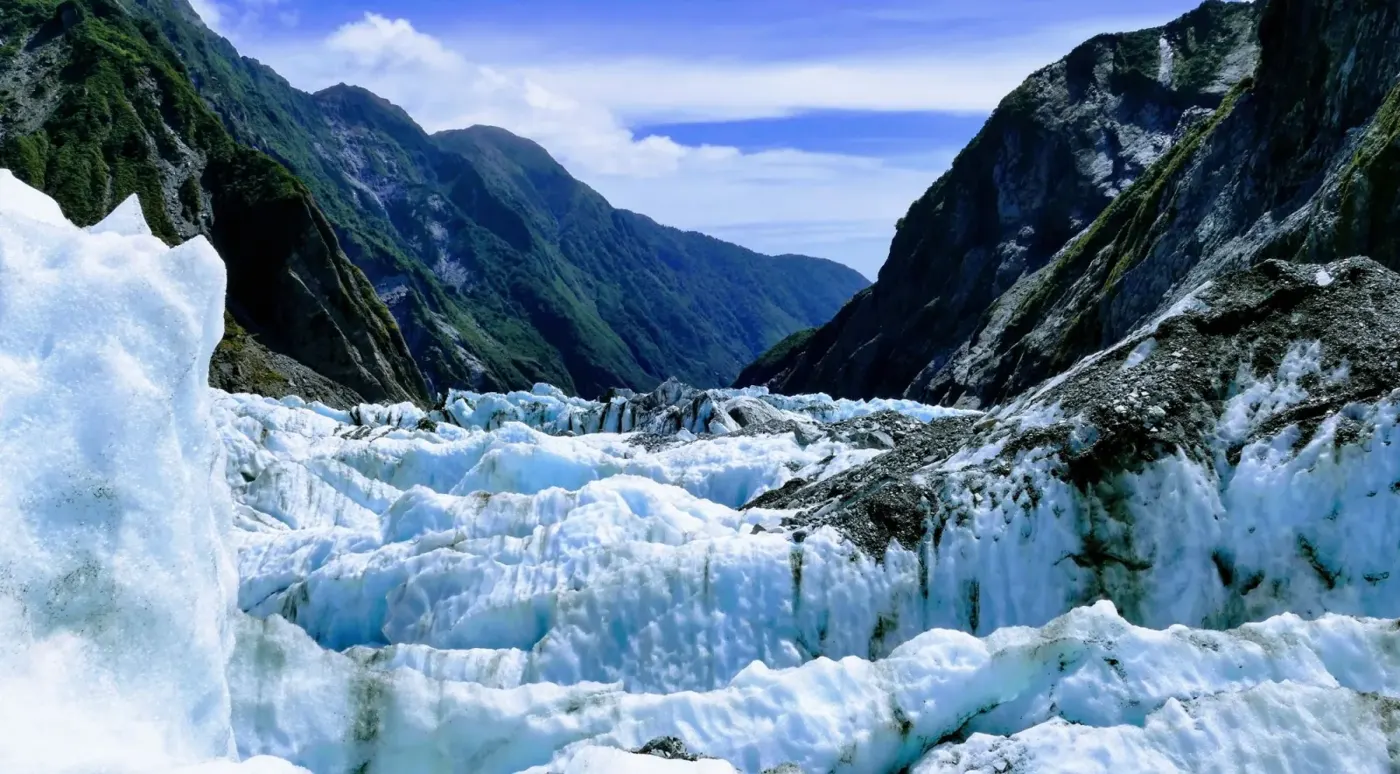 Glacier ice opening towards a green mountain valley