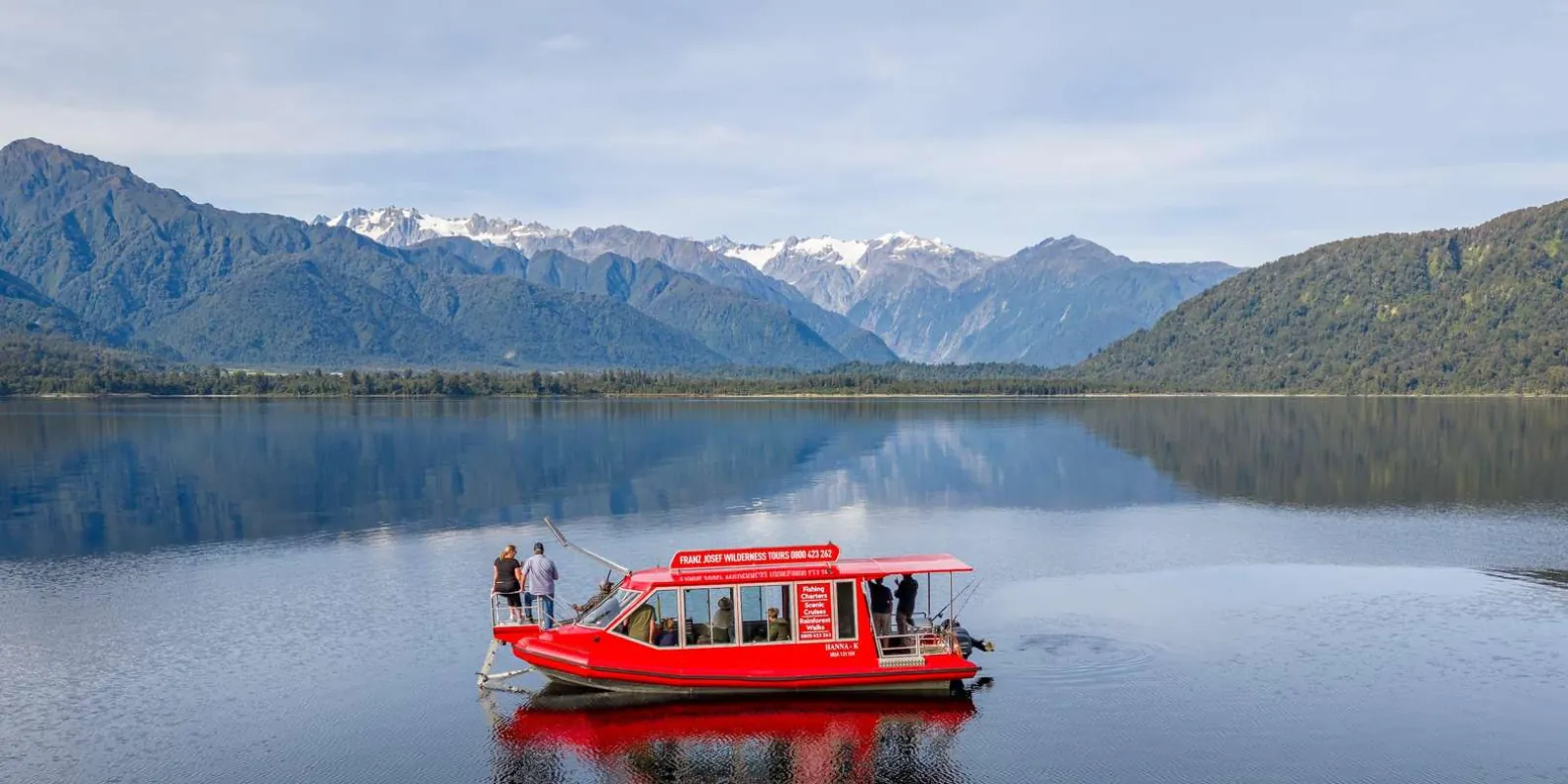 Red cruise boat on Lake Mapourika with mountains behind