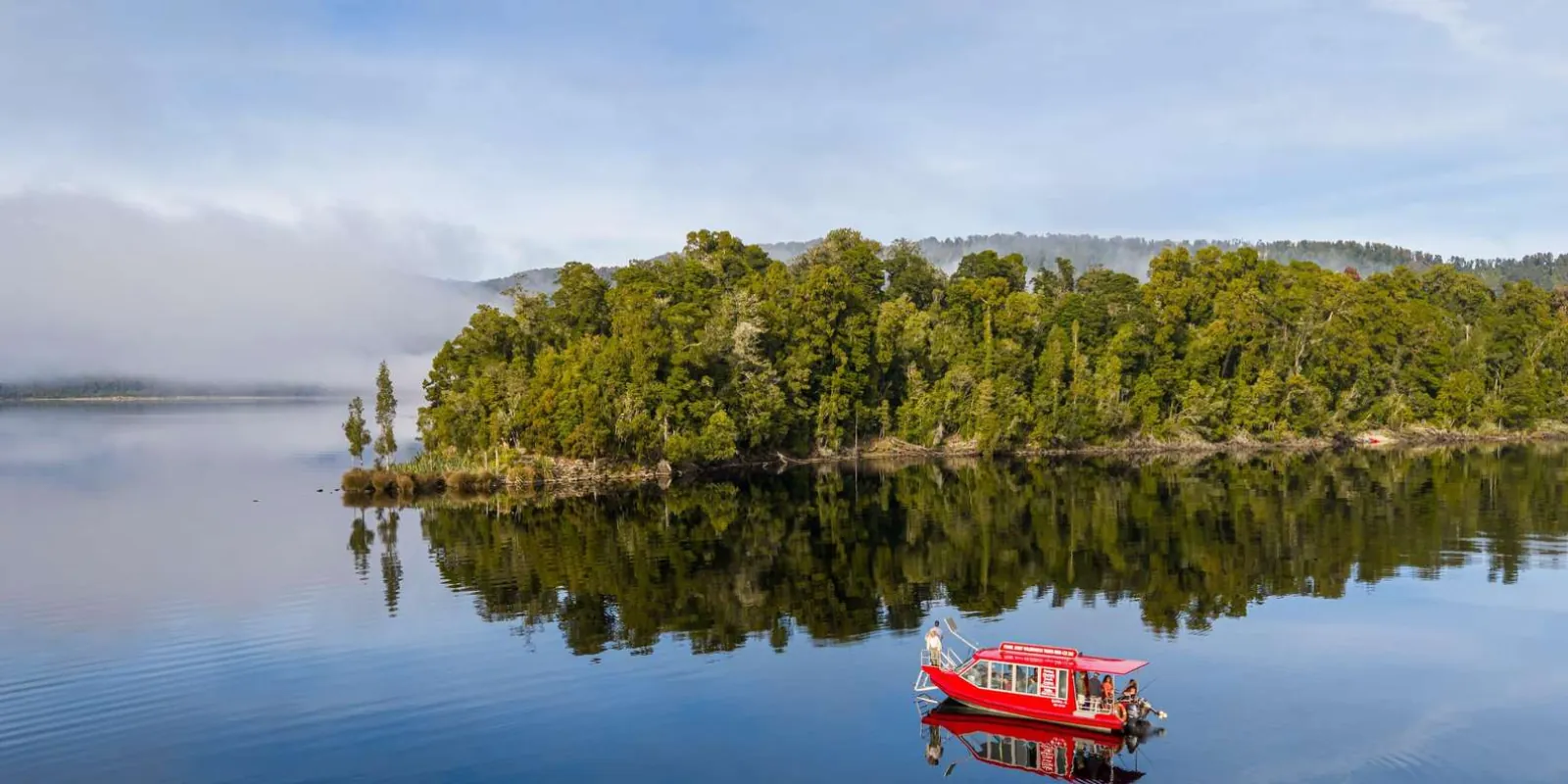 Red boat beside a wooded lake shoreline