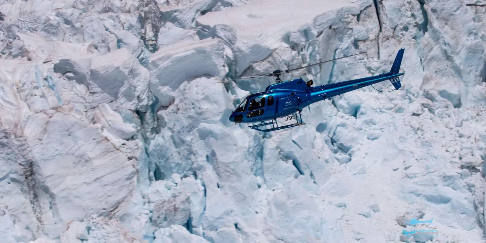 Blue helicopter flying above glacier ice